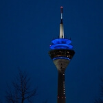 Der Rheinturm, ein Wahrzeichen Düsseldorfs, leuchtet nachts blau.