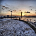 Eine Person steht im Winter auf einem Pier mit einer Brücke im Hintergrund.