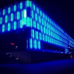 Ein blaues Gebäude, das nachts von Lichtkunst beleuchtet wird.