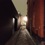 Eine schmale Kopfsteinpflasterstraße in Gent bei Nacht, während ein Zug die Straße entlangfährt.