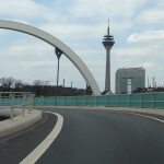 Eine Brücke über eine Autobahn mit Fernsehturm und Stadttor im Hintergrund.