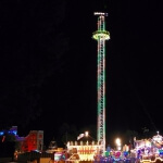 Ein Riesenrad thront über der Landschaft und ist nachts beleuchtet.