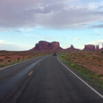 Ein Kraftfahrzeug fährt eine leere Straße im Monument Valley entlang.