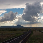 Ein regnerischer, bewölkter Himmel über einer Autobahn mit Bergen im Hintergrund.