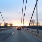 Ein Auto fährt bei Sonnenuntergang eine Autobahn entlang und überquert eine Brücke.