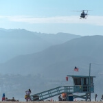 Ein Hubschrauber fliegt mit einem Rettungsschwimmerturm über den Strand von Santa Monica.