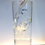 Links wird ein Glas Wasser in ein Glas gegossen.
