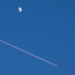 Ein Flugzeug mit einer Spur von Kondensstreifen am Himmel, in der Nähe des Mondes.