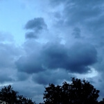 Ein bewölkter Himmel mit Wolken und Bäumen im Hintergrund.