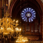 Ein goldener Kronleuchter in einer Kirche mit einem Buntglasfenster.