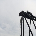 Eine schwarze Achterbahn im Heidepark Soltau, im Hintergrund ein bewölkter Himmel.