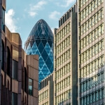 Ein hohes Gebäude mit spitzer Spitze und der außerirdischen eiförmigen 30 St Mary Axe im Hintergrund.