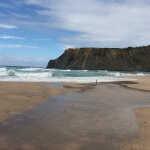 Ein Strand mit Wellen der Marke Wellen und Klippen im Hintergrund.