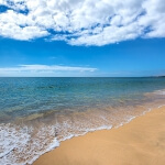 Ein Sandstrand in Portugal mit blauem Himmel und Wolken.