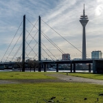 Eine Brücke über einen Fluss in Düsseldorf mit einem Fernsehturm im Hintergrund.