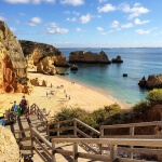 Ein Strand an der Algarve, Portugal, mit Treppen, die zum Wasser führen.