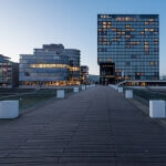 Ein Holzsteg neben dem Hyatt Düsseldorf in der Abenddämmerung.