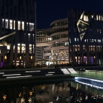 Eine Stadt bei Nacht mit den Düsseldorfer Kö-Bogen II-Gebäuden und einem Teich.