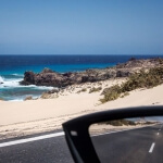 Im Rückspiegel eines Autos blickt man zurück auf das Meer und die Sanddünen.
