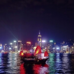 Nachts schwimmt ein Boot im Wasser und bewundert die Skyline von Hongkong.