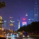 Skyline von Shanghai bei Nacht mit Autos, die die Straße von Shanghai entlangfahren.