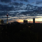 Eine Stadt in der Abenddämmerung mit einem Fernsehturm im Hintergrund und dem atemberaubenden Sonnenuntergang Düsseldorfs.