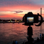 Eine Kamera steht auf einem Stativ vor einem Fluss beim Sonnenuntergang der Rheinkirmes in Düsseldorf.