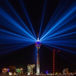 Der Düsseldorfer Fernsehturm Rheinturm wird nachts mit blauen Lichtstrahlen beleuchtet.