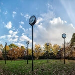 Eine Gruppe von Uhren in einem Park, die verschiedene Zeitzonen anzeigen, mit Bäumen im Hintergrund.