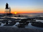 Ein Leuchtturm Obereversand steht bei Sonnenuntergang am Ufer.