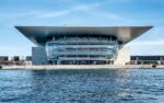Ein modernes Operngebäude mit Glasdach auf einem Gewässer in Kopenhagen, Dänemark.