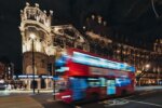 Ein Doppeldeckerbus fährt nachts an einem Gebäude in der Londoner City vorbei.