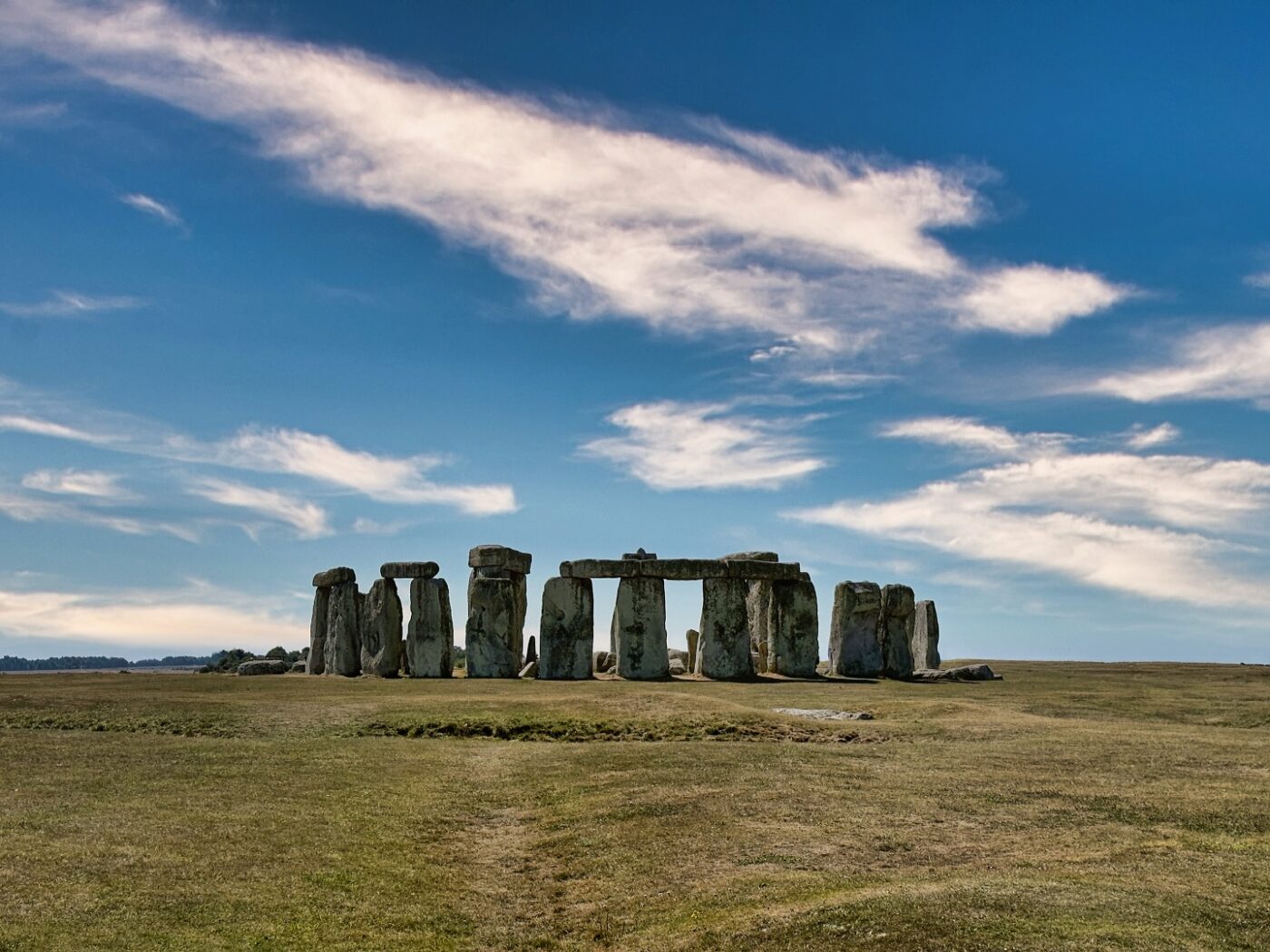 Stonehenge erhebt sich auf einer offenen Grasebene unter einem blauen Himmel mit vereinzelten Wolken.
