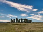 Stonehenge erhebt sich auf einer offenen Grasebene unter einem blauen Himmel mit vereinzelten Wolken.